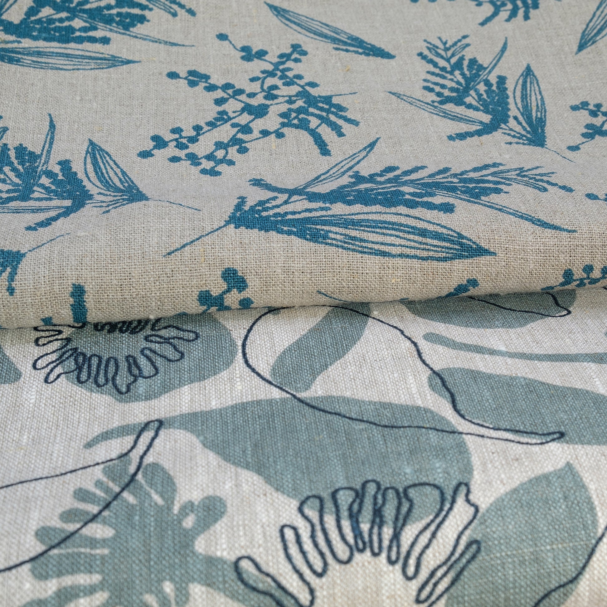 Linen fabric hand screenprinted with seedpods design in storm and indigo colour on oatmeal linen and mixed wattle design in sea blue on a flax linen. Designed and printed by Femke Textiles.
