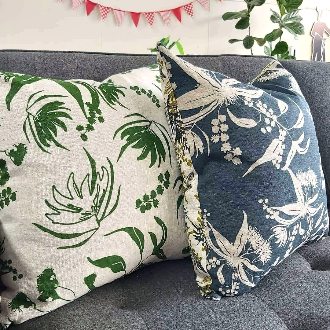 A linen cushion cover featuring mixed wattle print in olive oil and indigo and Forager's Delight print in indigo plus a cushion cover featuring Local Forage print in envy. Designed and printed and made by Femke Textiles.